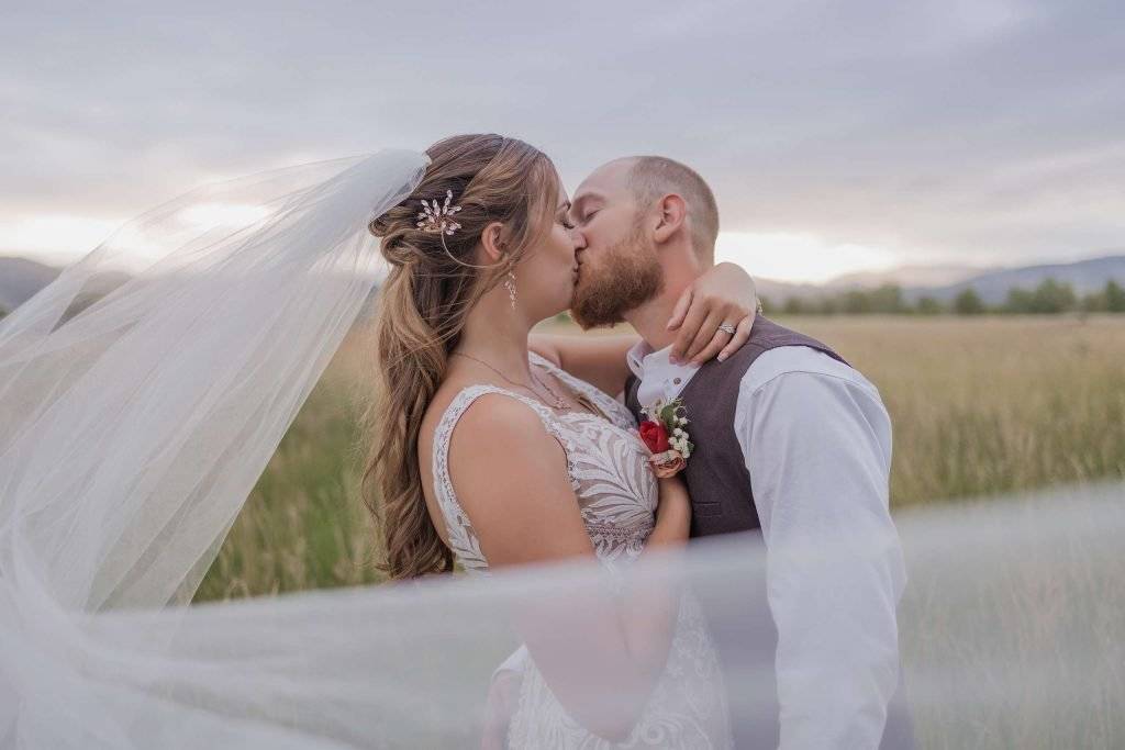 A bride and groom kissing in a field with a veil in Colorado