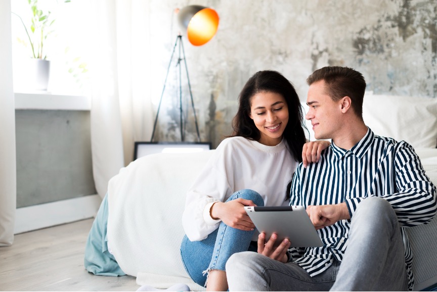 A bride and groom plan a wedding by reading an ebook together on the couch.