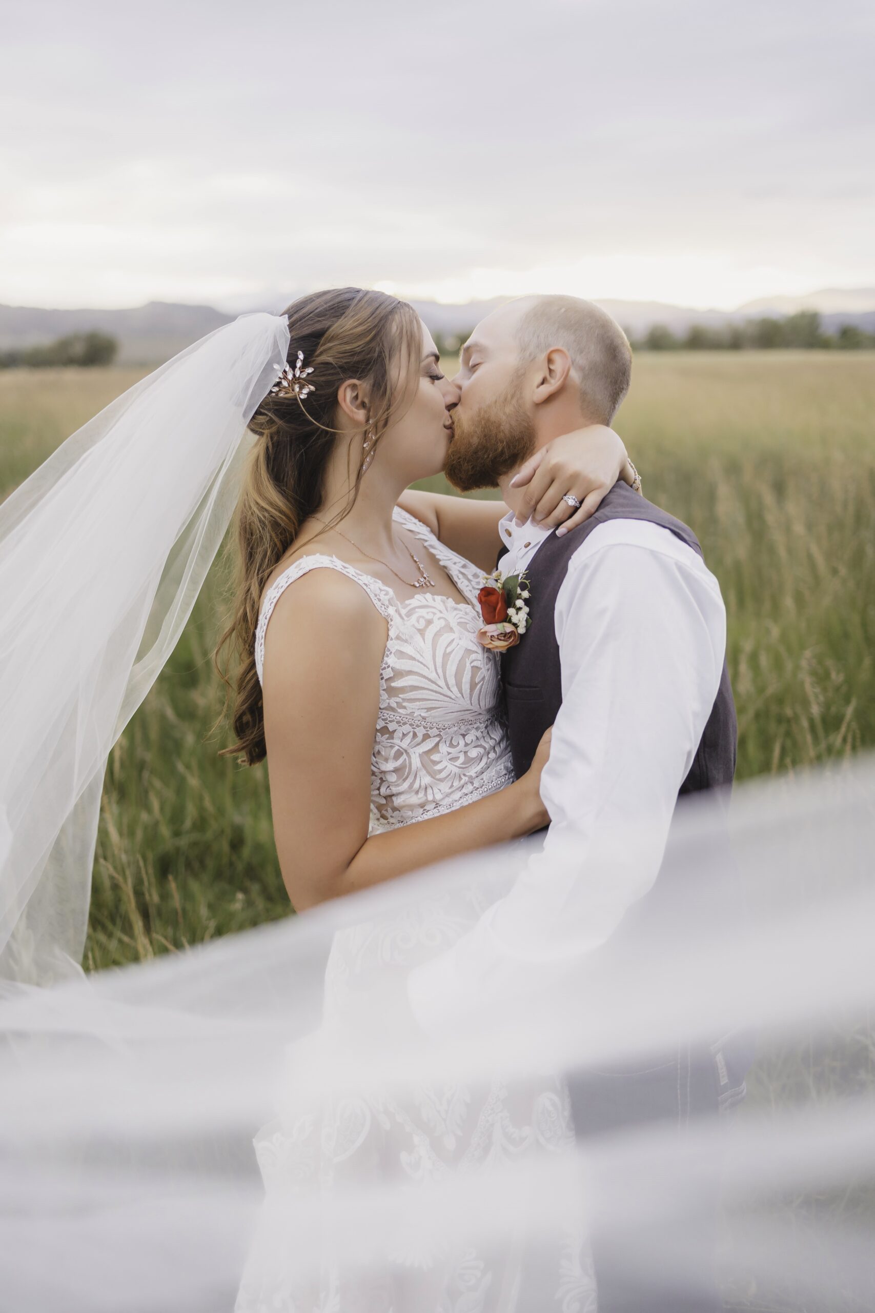 A bride and groom kiss with a bridal veil in a field in Colorado.