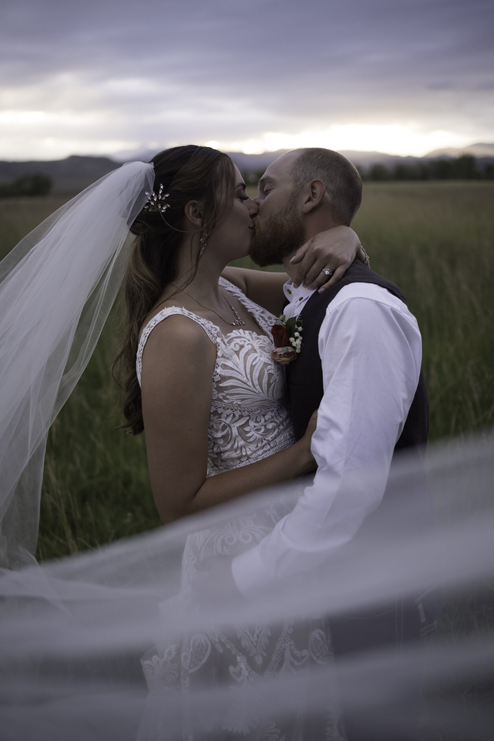 a bride and groom kissing field kissing under a veil in Colorado.