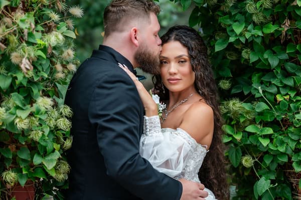 A bride and groom share an intimate moment amidst lush greenery in a serene outdoor garden setting.