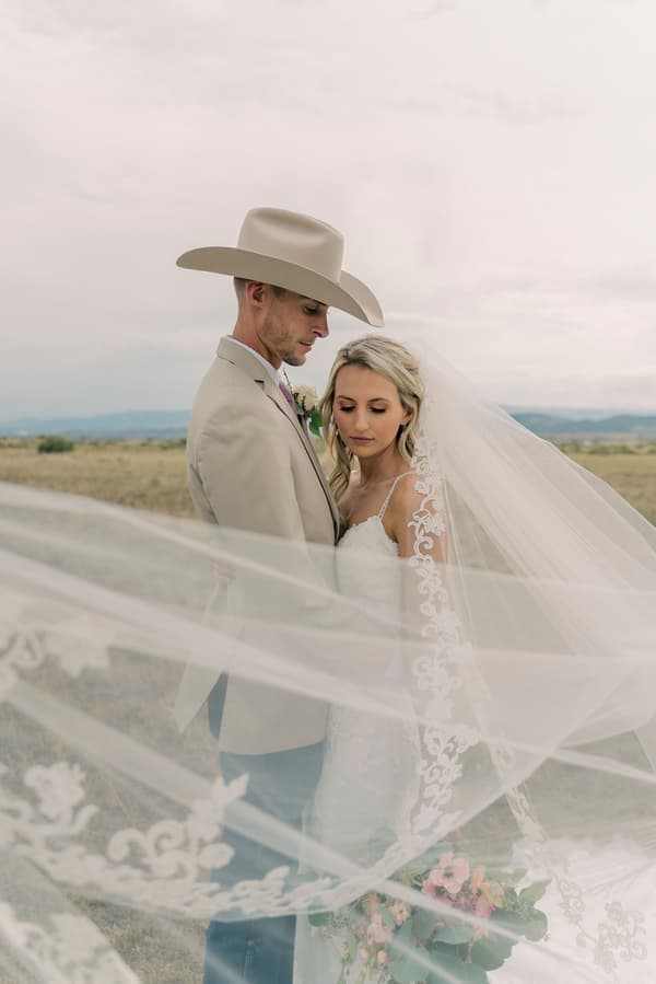A bride and groom share a tender moment under an expansive sky in a rural setting.