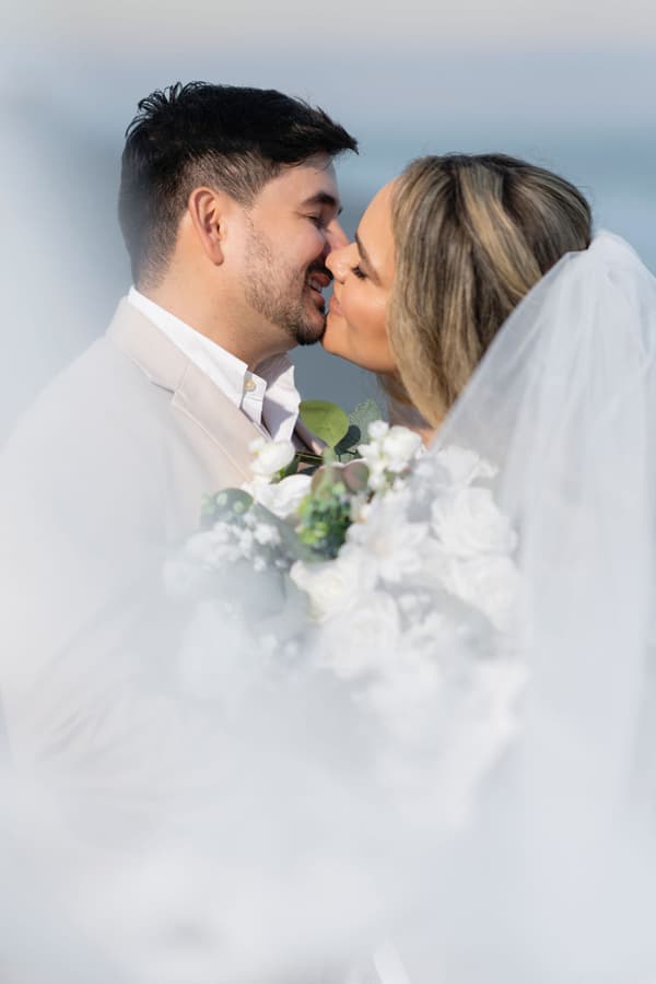 A bride and groom share a tender kiss against a soft, ethereal backdrop of misty clouds during golden hour.