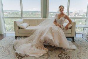 bride sitting on a white couch in front of a big bay window.