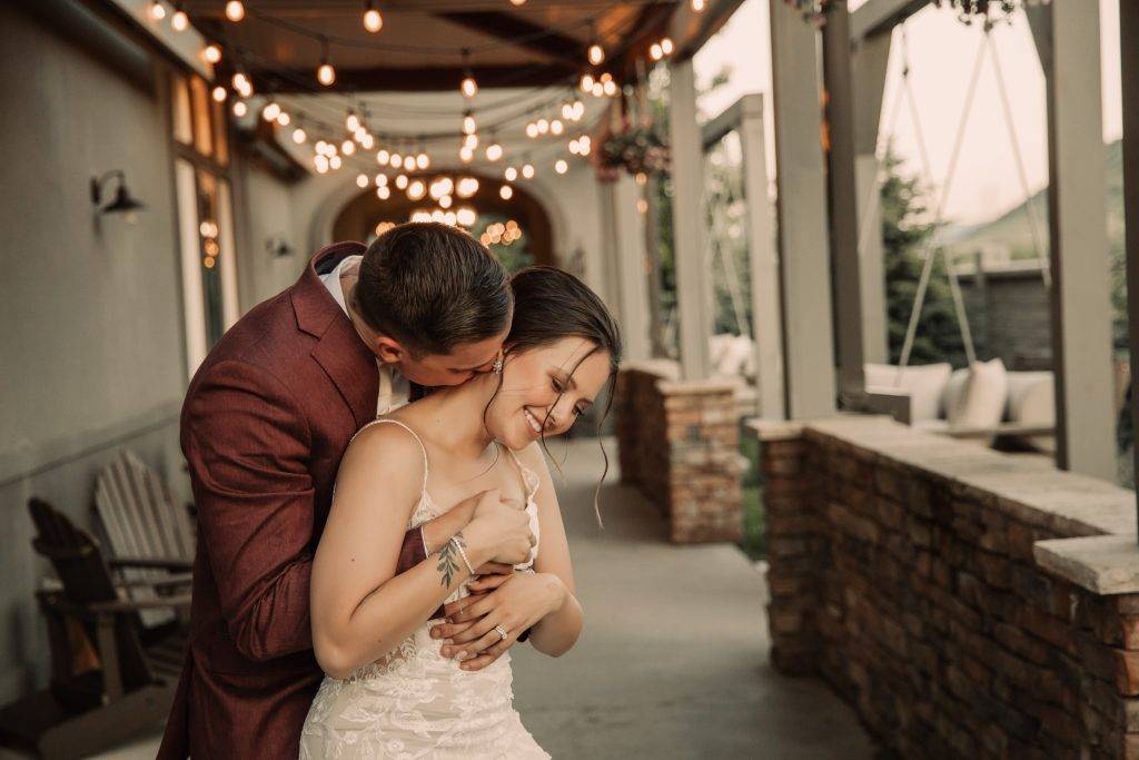 groom kissing brides neck down an alley with lights.