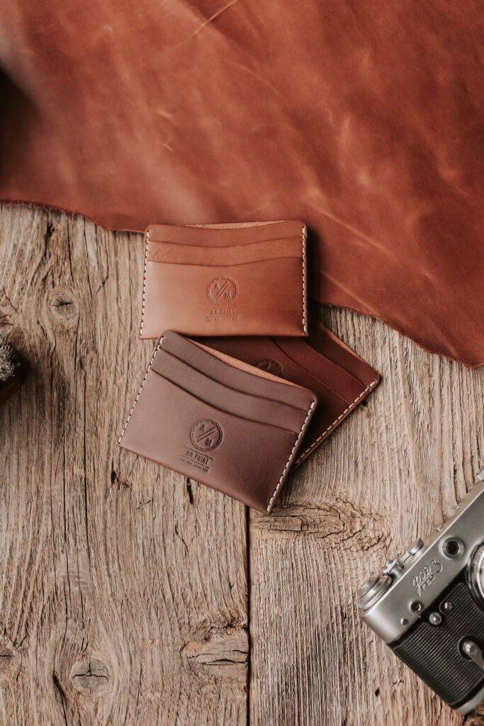 Professional Commercial Photographer images of 3 brown wallets laying on a wooden table with a camera next to them.