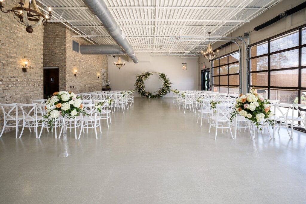 indoor wedding venue with white chair, big bay windows, and a green circle arch