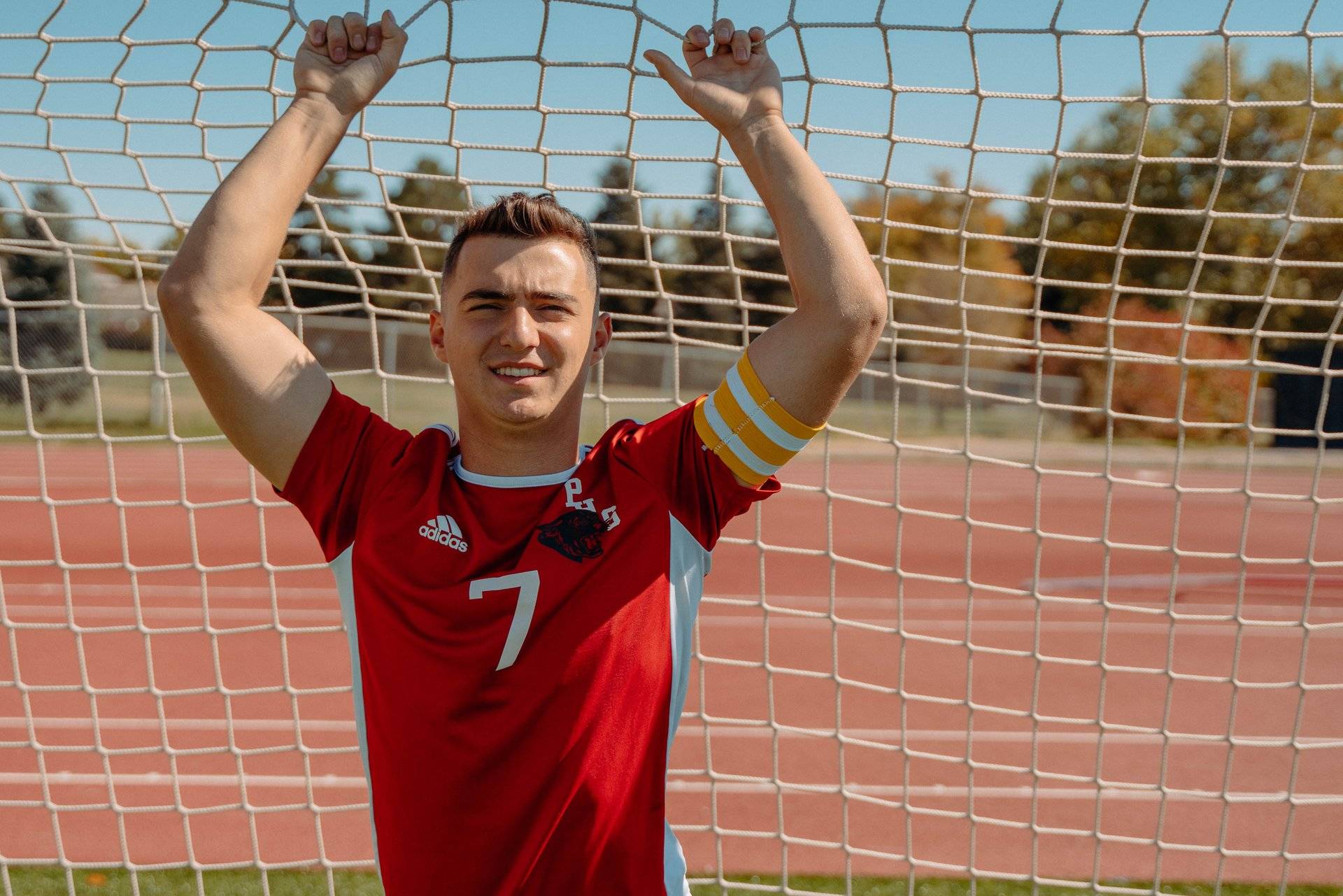 A senior standing in front of a soccer net with a soccer jersey on for senior photos.