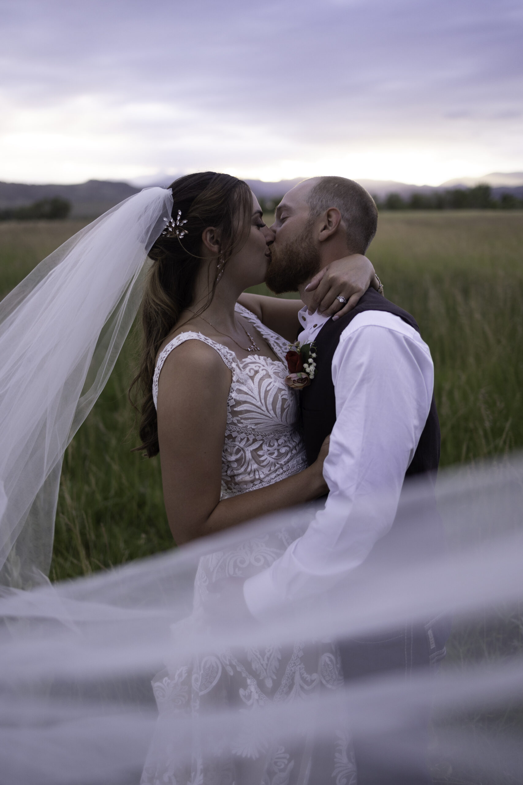 A bride and groom kiss with a bridal veil in a field in Colorado.